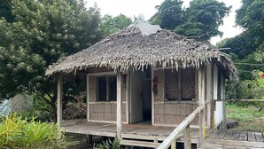 A small wooden structure with a thatched roof, a wooden deck, and a single door. - White Beach Bungalow  (Tanna Island)