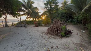 A beach with sand, palm trees, and a small pile of sticks. - White Beach Bungalow  (Tanna Island)