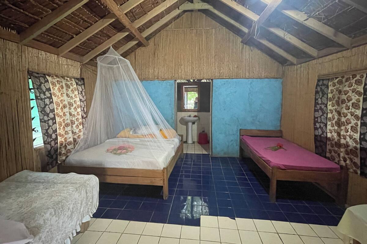 A room with a wooden ceiling, a bed with a canopy, a small table, and a bench.