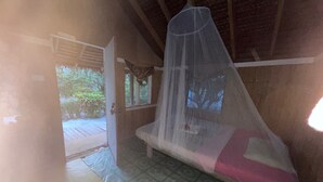 A room with a bed under a mosquito net, a door leading outside, and patterned flooring. - White Beach Bungalow  (Tanna Island)
