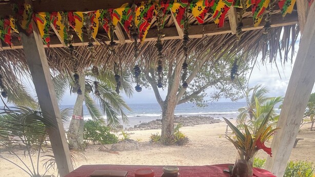 A beachside dining setup with a table covered by a red cloth, plates with food, and a view of the ocean. - White Beach Bungalow  (Tanna Island)