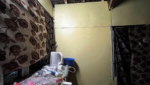 A small, dimly lit room with a bed, a table with various items, and a curtain with a floral pattern. - White Beach Bungalow  (Tanna Island)