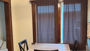 A dining area with a wooden table and chairs, a ceiling fan, and large windows with curtains.