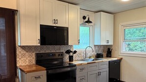 A modern kitchen with white cabinets, a black stove, and a window with a view of greenery.