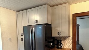 A compact kitchen with a stainless steel refrigerator, white cabinets, a wooden countertop, and a coffee maker.