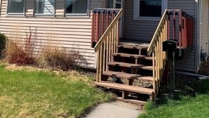 A single-story house with a front porch, a small staircase, and a window with shutters.