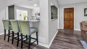 A dining area with a kitchen in the background, a wooden door, and a brown leather chair. - Big Mtn Home, Dog & Kid Friendly, close to Biltmore, breweries, & orchards (Hendersonville)
