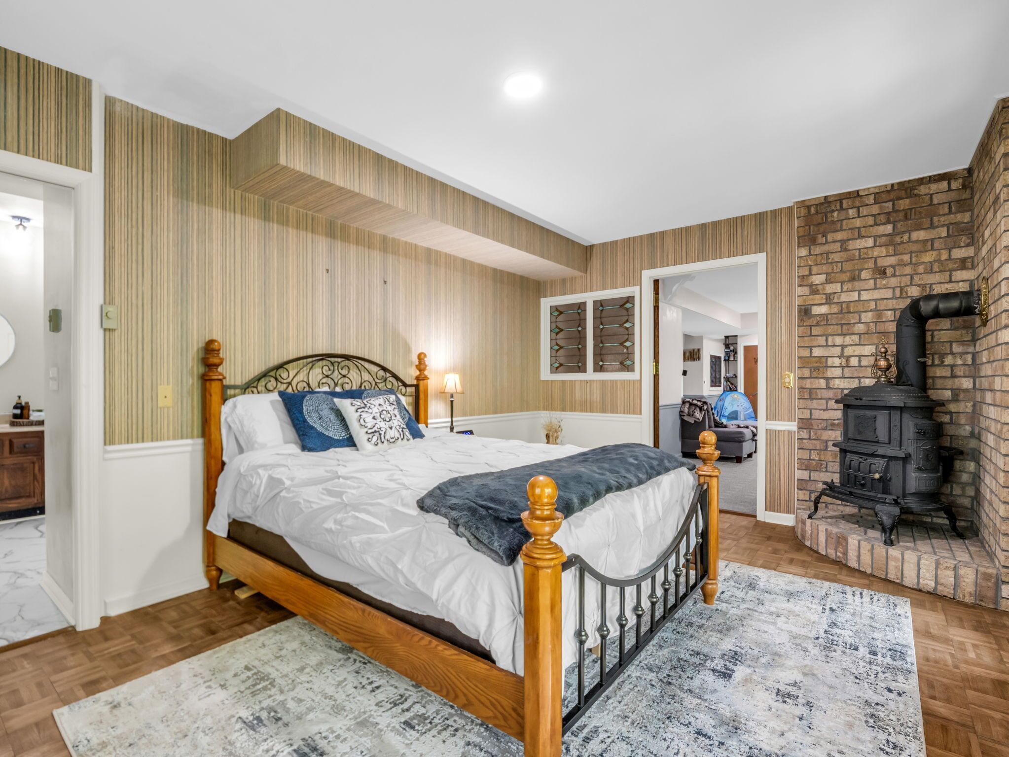 Une chambre avec un lit en bois, un tapis à motifs, un mur en briques et un poêle à bois.