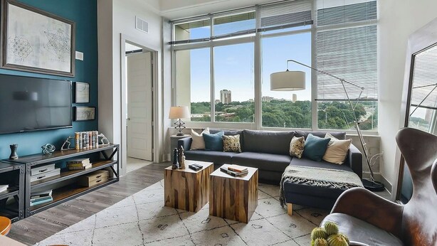 Una sala de estar moderna con un ventanal grande, un sofá, dos mesitas de madera y un televisor sobre una estantería.