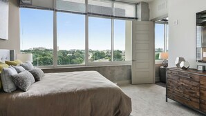Un dormitorio con una ventana grande, una cama, un aparador y una puerta.