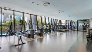 Un gimnàs modern amb màquines cardiovasculars, una panca de peses i grans finestres que ofereixen vistes a la ciutat.