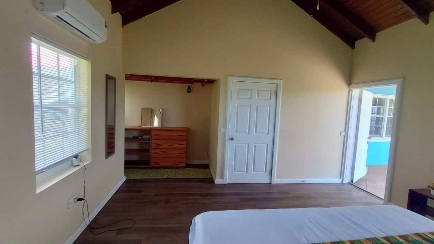 A bedroom with a bed, a dresser, a door, and a window.