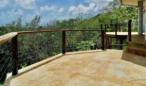 Un balcon doté d’une rambarde en métal, d’un sol carrelé et offrant une vue sur la verdure.