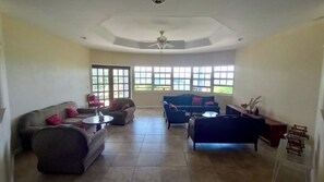Ein geräumiges Wohnzimmer mit hohen Decken, großen Fenstern und einem Deckenventilator.