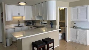 A kitchen with white cabinets, a countertop, a sink, a microwave, and two stools. - Penthouse level Waikiki Gold Coast- Spectacular Ocean View (Honolulu)