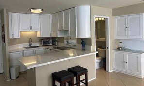 A kitchen with white cabinets, a countertop, a sink, a microwave, and two stools. - Penthouse level Waikiki Gold Coast- Spectacular Ocean View (Honolulu)