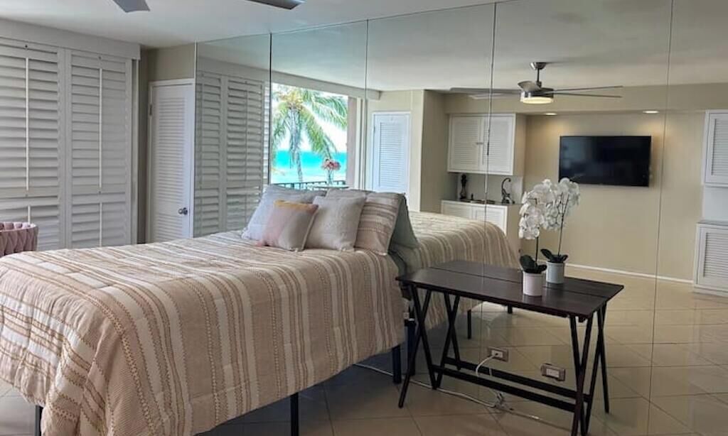 Quarto com cama, mesinha, televisão e vista para o oceano.
