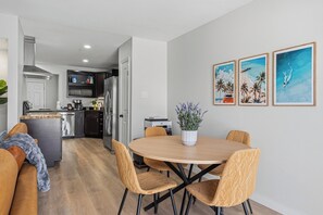 Uma cozinha moderna com uma ilha central, uma área de refeições com uma mesa redonda e cadeiras, e uma sala de estar com sofá e mesa de centro.