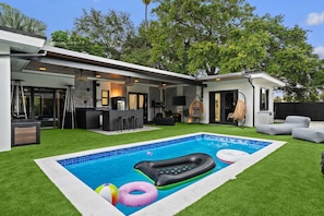 A modern outdoor pool area with a built-in bar, seating, and a well-maintained lawn. - Beautiful 2BR/2BA Oasis with Pool, Gym & Private Parking (Miami)