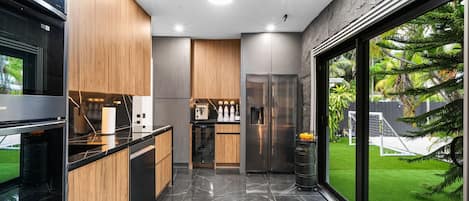 Une cuisine moderne dotée d’un îlot central, d’appareils électroménagers intégrés et d’une grande fenêtre donnant sur une pelouse verdoyante.