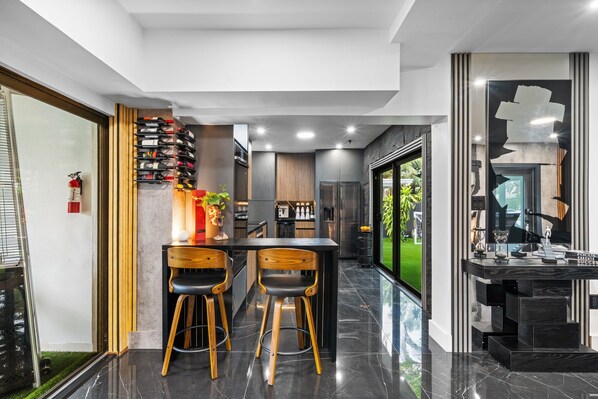 A modern kitchen with a bar area, two wooden bar stools, a wine rack, and a view of the outdoors.