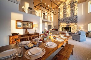 A dining area with a long wooden table set for a meal, a stone fireplace, and a cozy living space with a sofa and striped armchairs. - The Loon at Intermediate | Pets | Hot Tub | Golf (Bellaire)