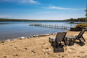 A lakeside beach with a dock, lounge chairs, and a small table.