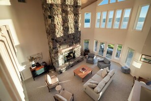 A spacious living room with a stone fireplace, a large window overlooking a body of water, and a cozy seating area. - The Loon at Intermediate | Pets | Hot Tub | Golf (Bellaire)
