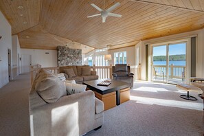 Ein geräumiges Wohnzimmer mit hoher Decke, einer Steinwand und Blick auf ein Gewässer durch große Fenster.
