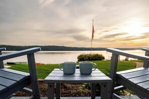A view from a deck with two chairs and a table, overlooking a body of water and a flag. - The Loon at Intermediate | Pets | Hot Tub | Golf (Bellaire)