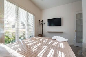 Un dormitorio con una cama, un televisor montado en la pared y una ventana con persianas.