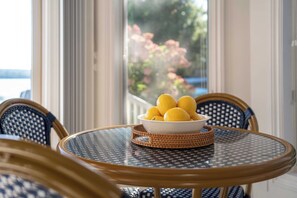 Ein runder Tisch mit einer Zitronenschale, Korbstühle und Blick auf einen Garten durch ein Fenster.