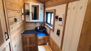Ein gemütlicher, kleiner Innenraum aus Holz mit einer Küchenzeile, einem kleinen Fenster und einer Dusche.