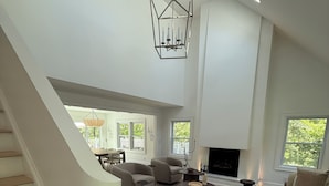 A spacious living area with a staircase, a fireplace, and a large window. - Luxury Hamptons Retreat, Heated Pool + Firepits (Water Mill)