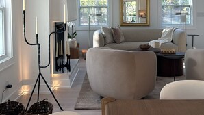 A modern living room with a sofa, a wooden coffee table, a floor lamp, and a large mirror. - Luxury Hamptons Retreat, Heated Pool + Firepits (Water Mill)