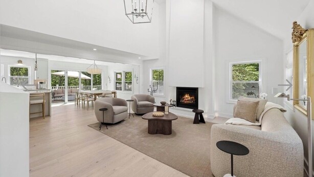 A spacious living room with a fireplace, a dining area, and a kitchen visible in the background. - Luxury Hamptons Retreat, Heated Pool + Firepits (Water Mill)