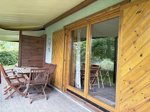 Eine Holzhütte mit überdachter Terrasse, einer Schiebetür und einem Tisch mit Stühlen.