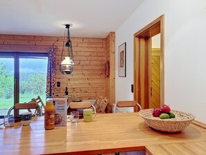 Ein Holzinterieur mit einem Esstisch, Stühlen, einer Hängelampe und Blick durch eine Glastür.