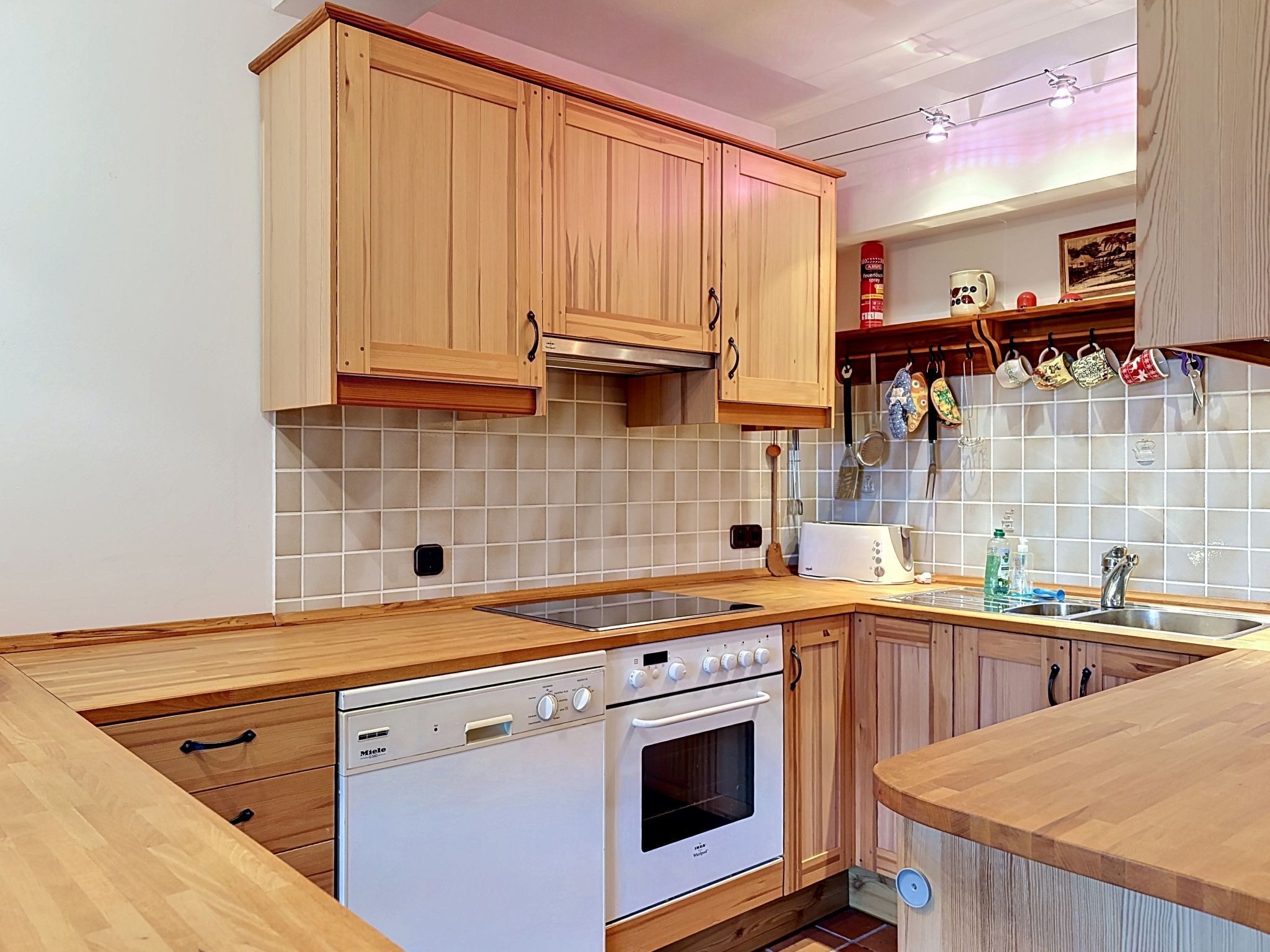 Una cocina con armarios de madera, lavavajillas, horno, pileta y salpicadero con azulejos.