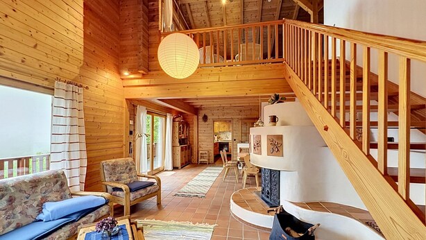 Un interior de madera con una escalera, un sofá, una mesa de comedor y vistas a través de una ventana.