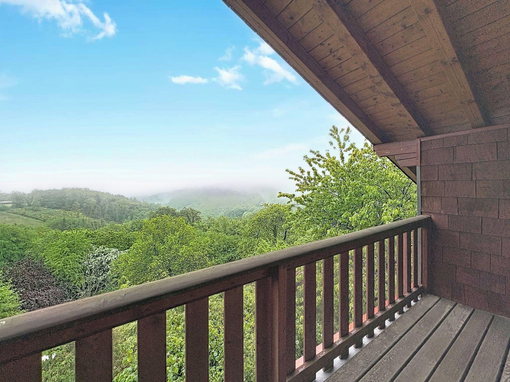 A balcony with a wooden railing overlooking a forested landscape.