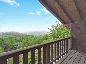 Un balcon doté d’une balustrade en bois, donnant sur un paysage boisé.