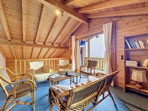 Un interior de madera con techo alto, muebles de mimbre, una estantería y vistas a través de una ventana.