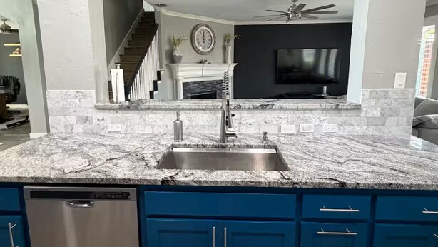 Une cuisine dotée d’un plan de travail en granit, de meubles bleus, d’un lave-vaisselle et d’une cheminée.