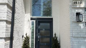 Une maison en briques blanches avec une porte bleu foncé, une grande fenêtre en arc de cercle et une boîte aux lettres portant le numéro 9610.