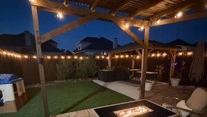 Une terrasse couverte avec un foyer, des sièges d’extérieur et des guirlandes lumineuses.