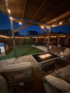 Eine überdachte Terrasse mit Feuerstelle, Sitzgelegenheiten im Freien und Lichterketten.