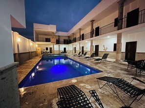 Un espace piscine avec des chaises longues et un bâtiment doté de nombreux balcons.