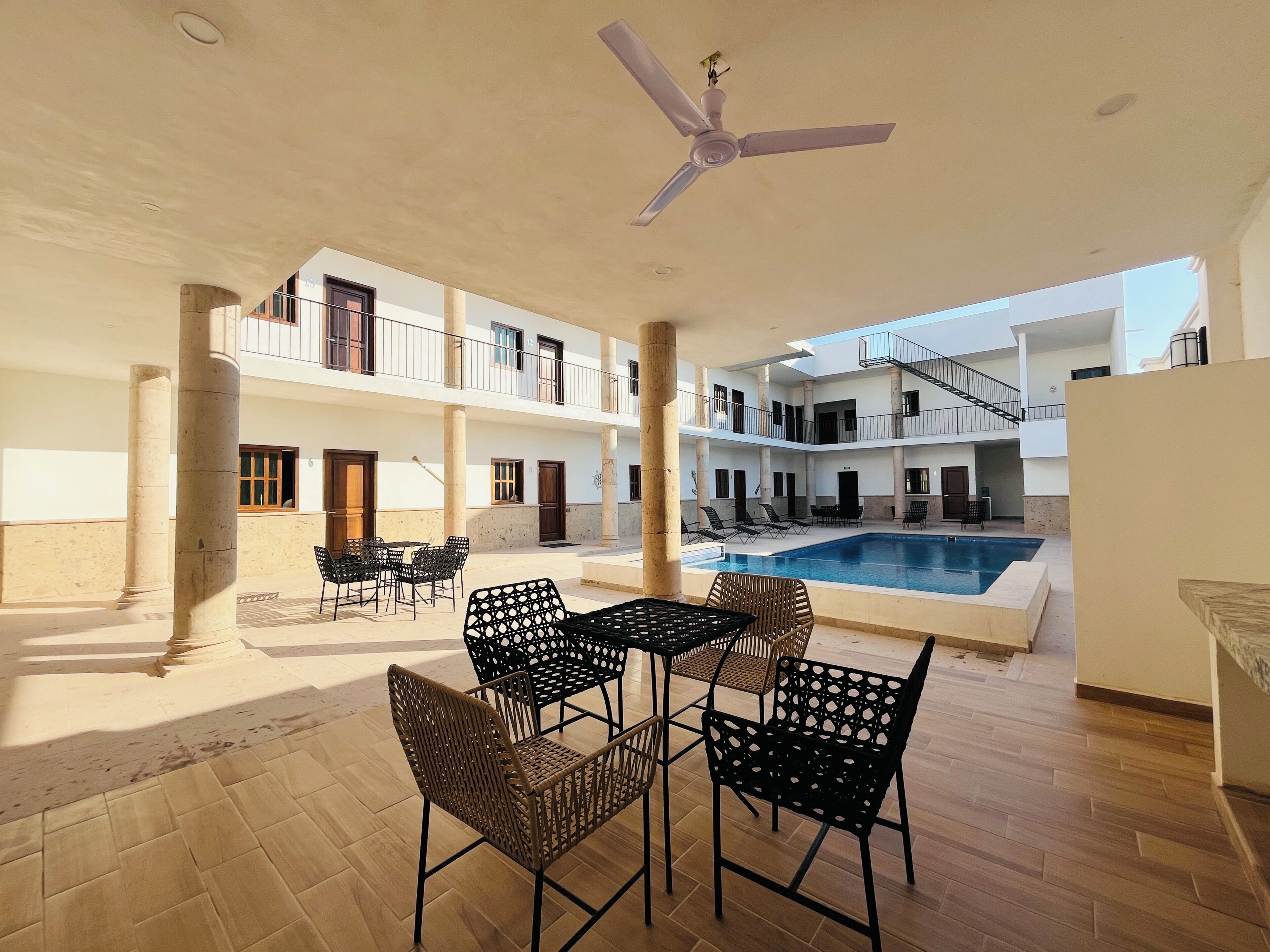 Un edificio de varios niveles con piscina, mobiliario de exterior y ventilador de techo.