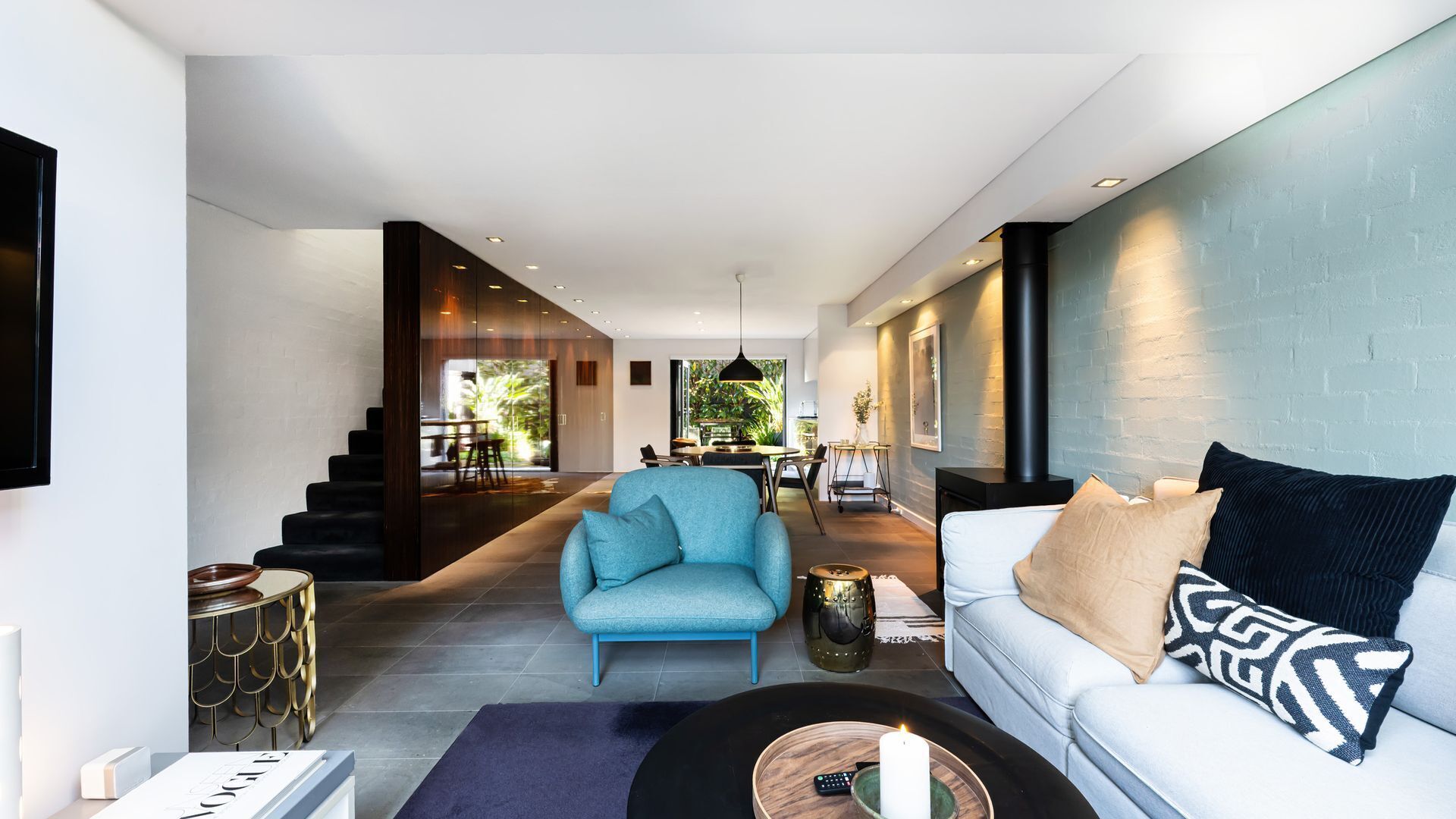 Un salon moderne avec un canapé, un fauteuil et une table basse. Un escalier mène à un autre niveau.